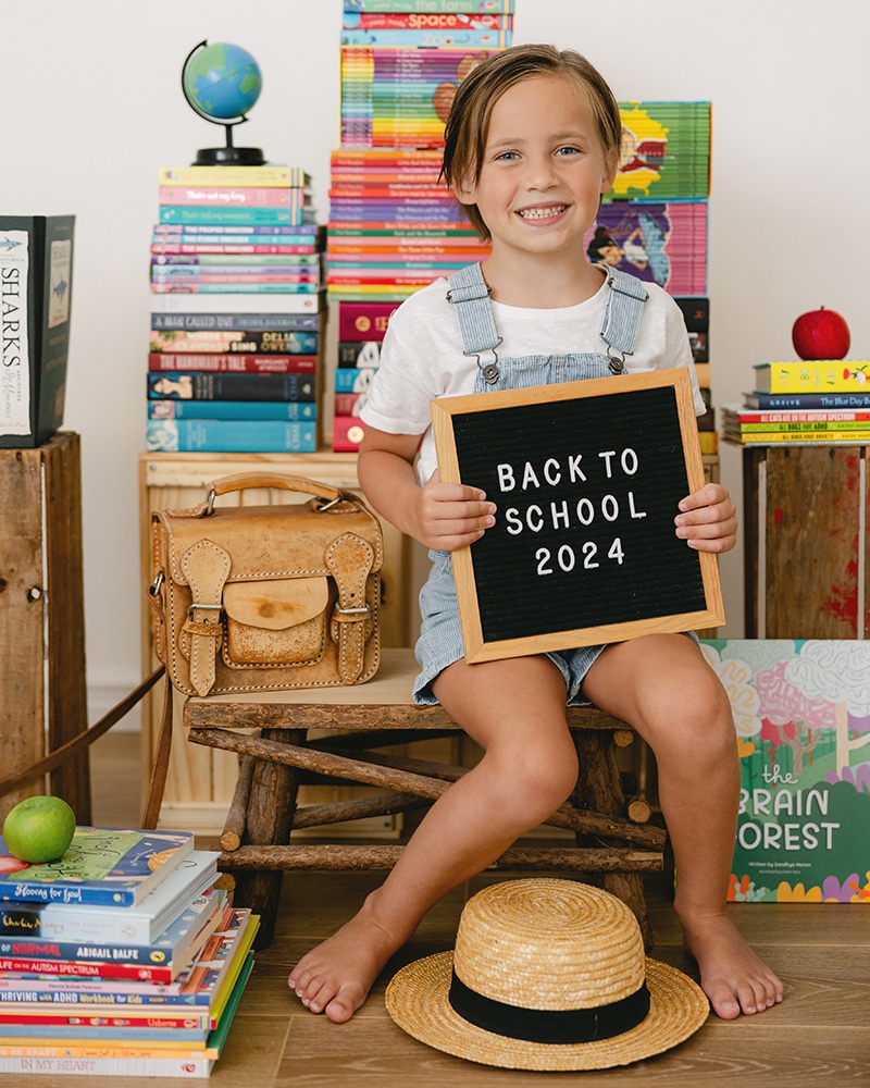 Boy surround by books with a sign saying back to school 2024