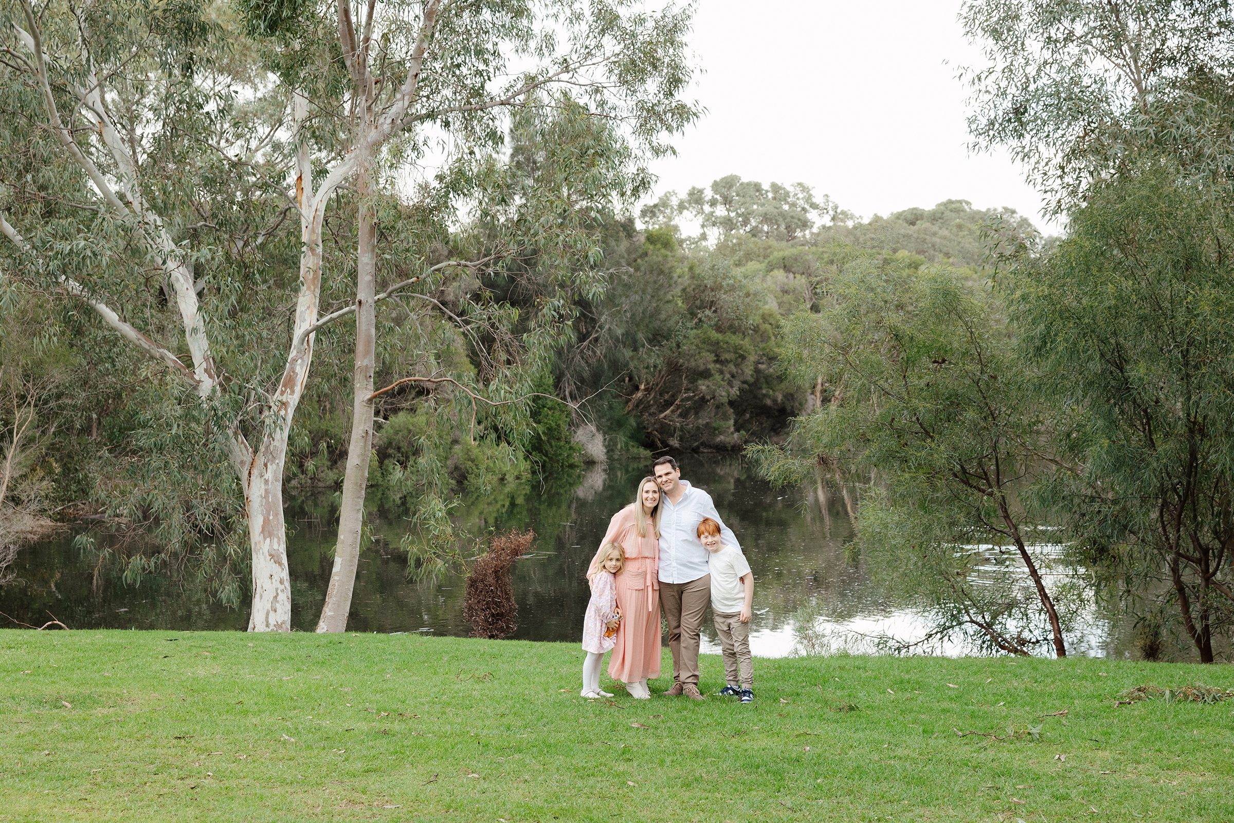 A family of four hugging on the grass at Carine Open Space
